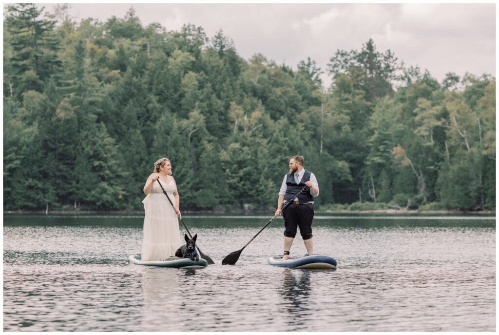 Bride and groom paddle boarding on a lake during their two-day adventure elopement in the Adirondacks.