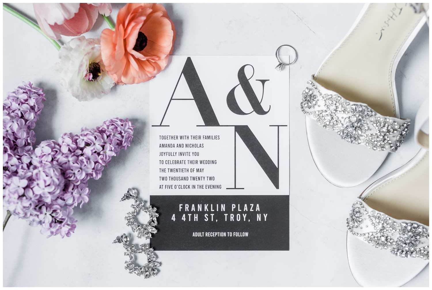 Black and white wedding invitation surrounded by bright flowers and other bridal details.