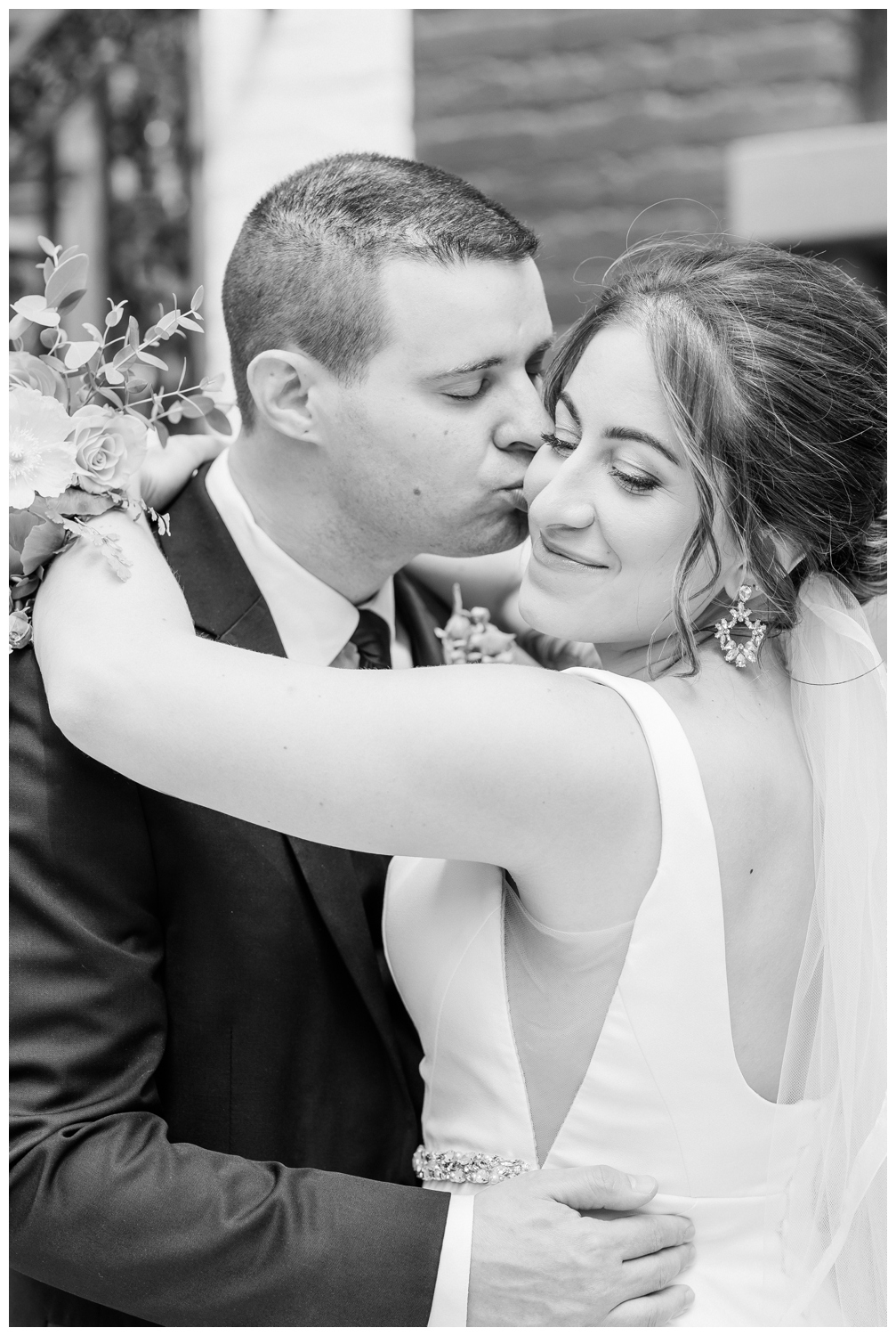 Black and white portrait of the Bride and Groom as he kisses her cheek.