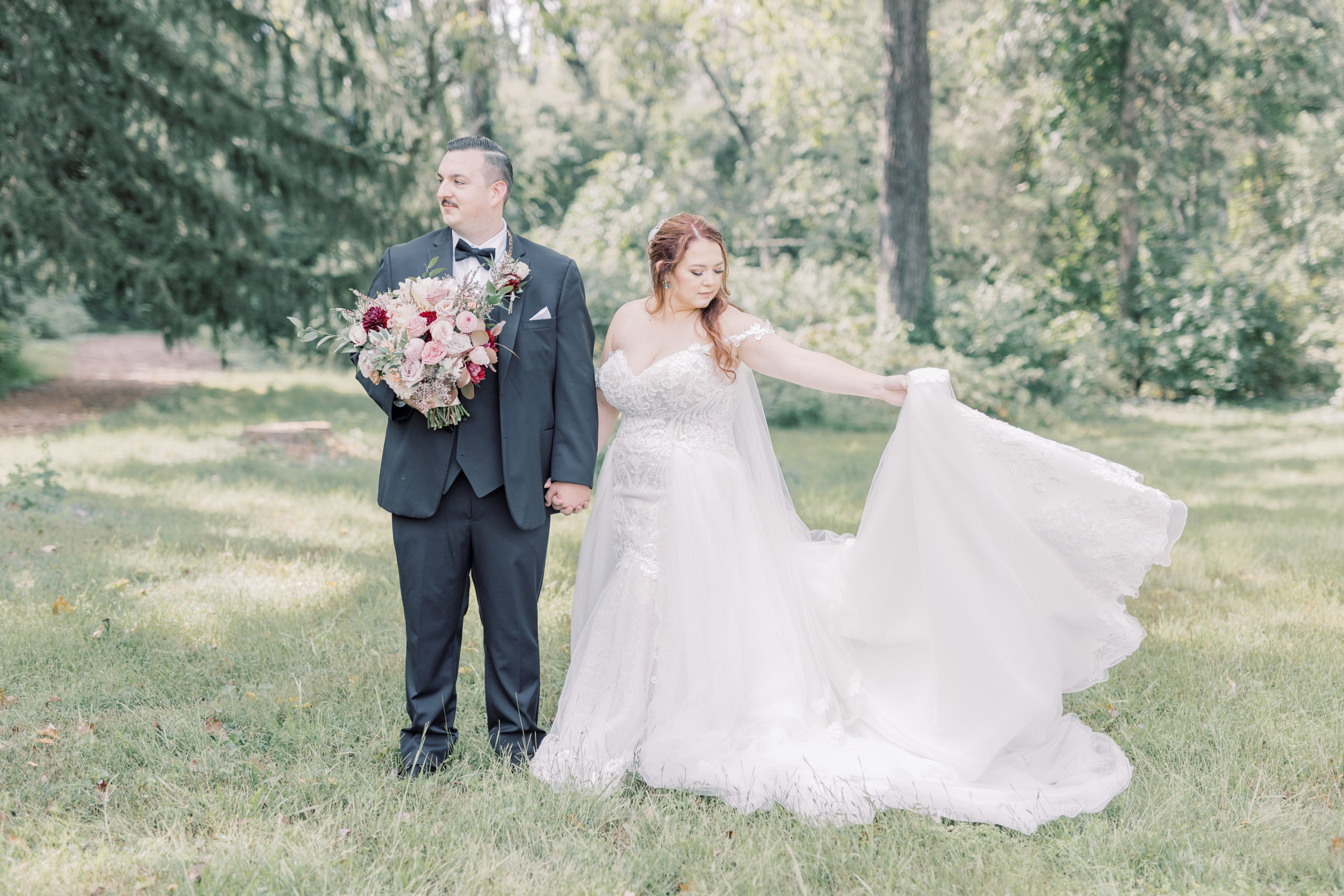 Bride and Groom standing next to each other in a tall grassy field holding hands on their wedding day. This light and airy wedding photo shows the bride spinning her dress while her groom holds her romantic bouquet of flowers. 