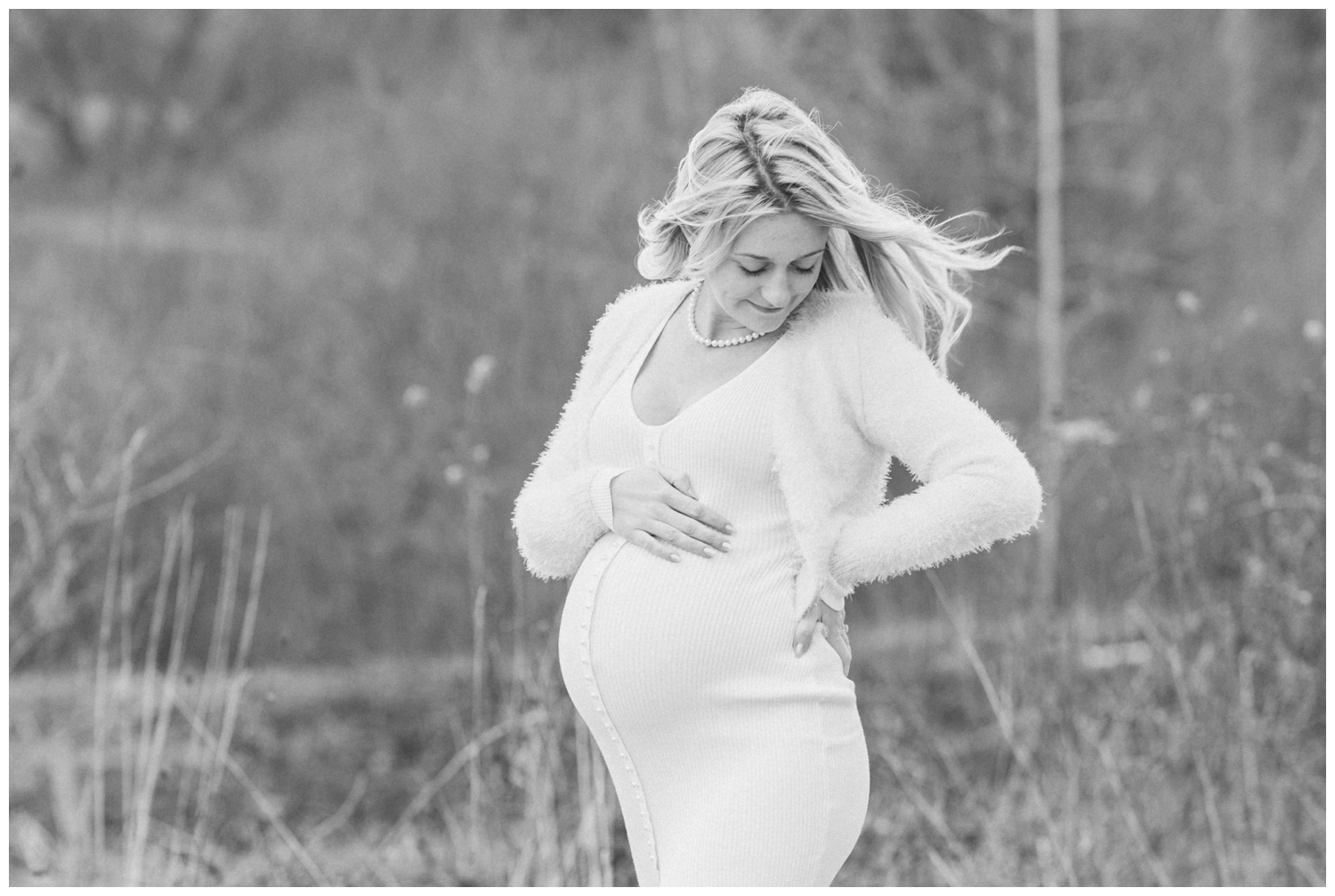 A black and white picture of a mom to be resting her hand on her pregnant belly while her hair blows gracefully in the wind in the mountains of the Catskills in New York.
