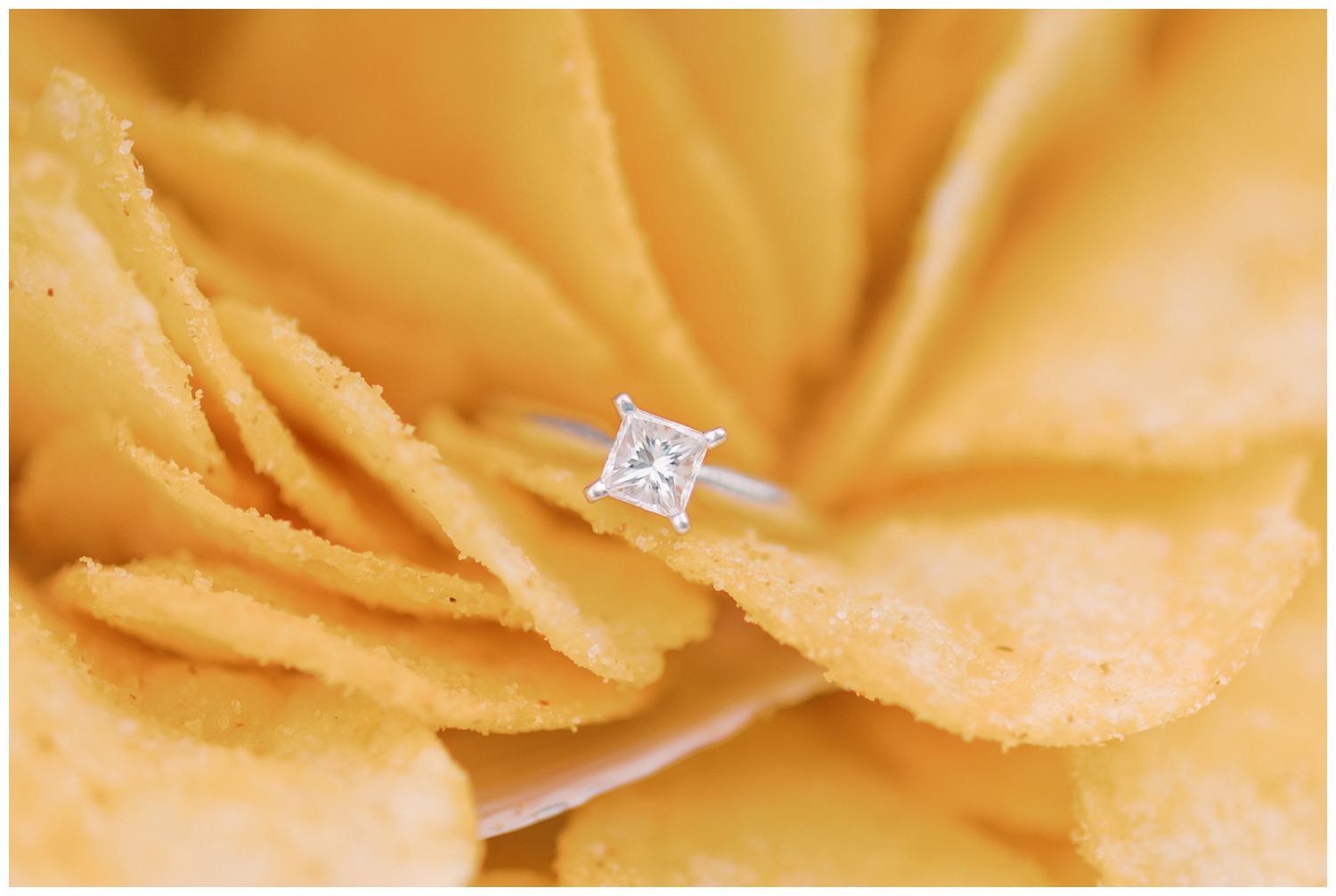 Macro shot of a diamond engagement ring in a bag of BBQ chips which is a favorite snack of the couple. 