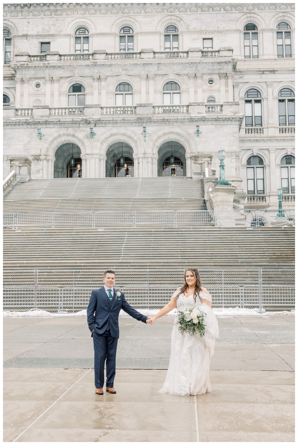 Bride and groom holding hands in front of the Capital Building in Albany, NY on their wedding day. They got married at The State Room on State Street in downtown Albany on a snowy March day.