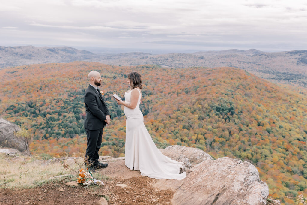 bride and groom exchaning vows on top of a cliff in the adirondacks with fall colored trees in the backdrop