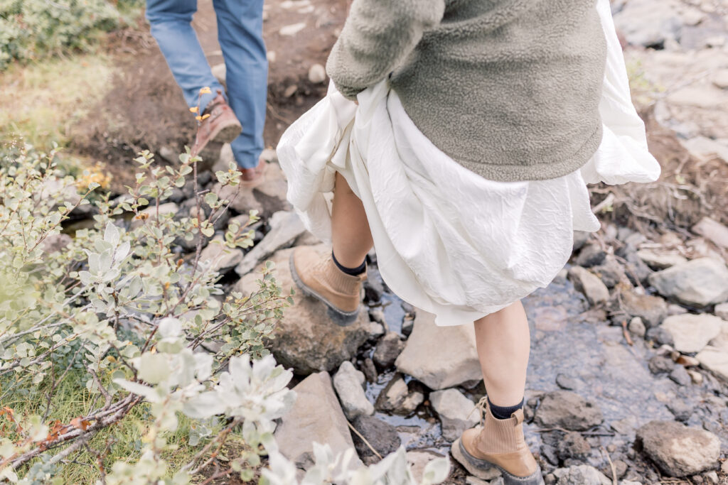 Bride lifting up hear dress while walking through a rocky creek wearing hiking boots.