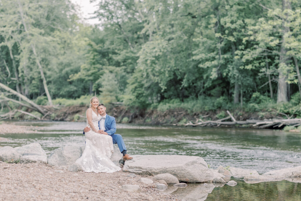 Bride and Groom sitting together by a river in Keene Valley during their Adirondack elopement.