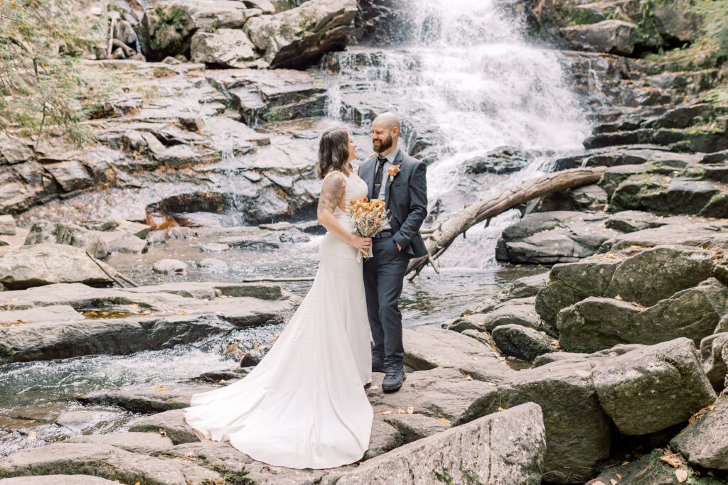 adventurous bride and groom elopement portrait in Adirondacks with waterfall in the backdrop