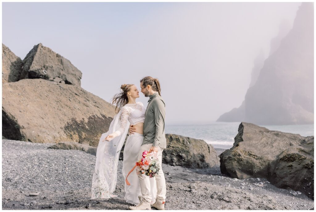 Couple about to kiss on black sand beach in Iceland during their elopement.