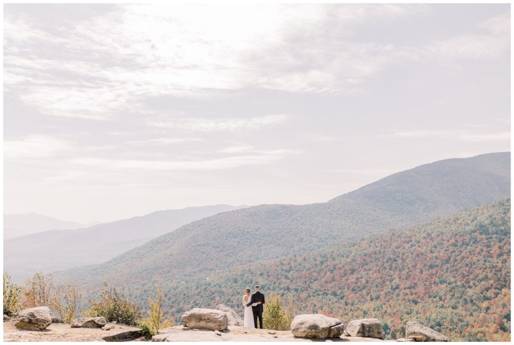 Bride and groom looking at the view of Fall foliage on top of a mountain.
