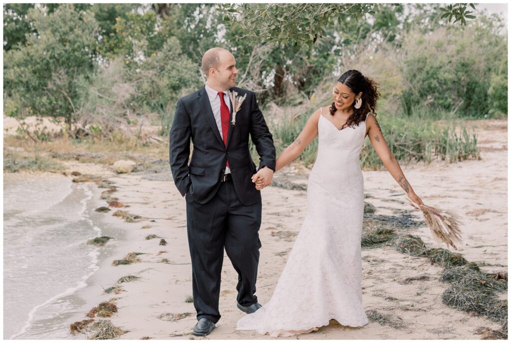 Bride and groom holding hands and walking on the beach.
