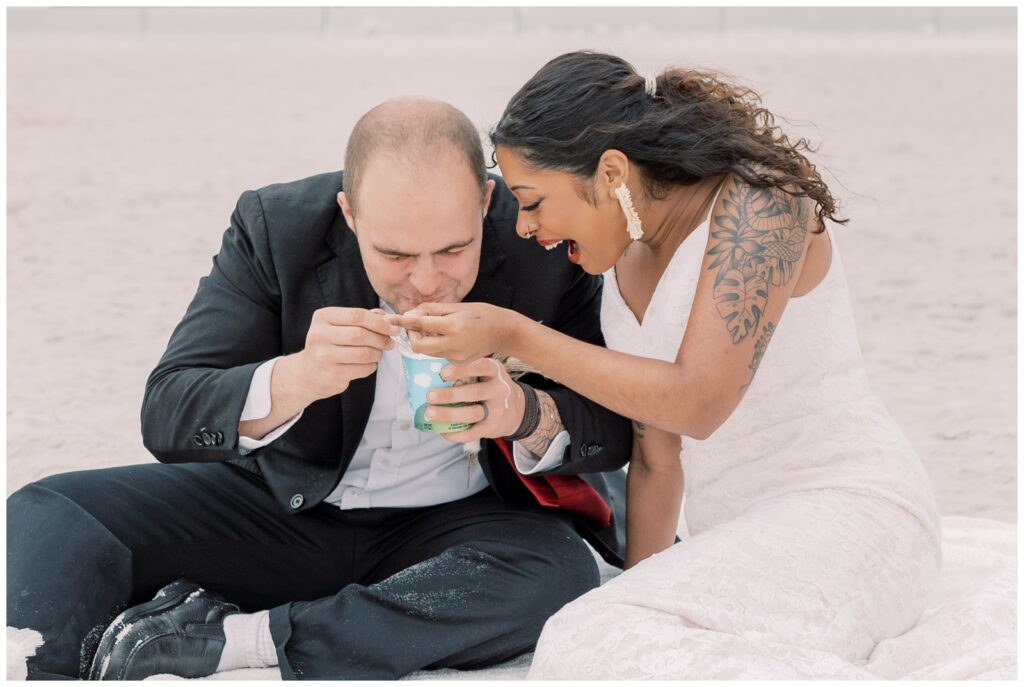 Couple sitting on a blanket on the beach in Crystal River, Florida, sharing a pint of melted ice cream on their wedding day.
