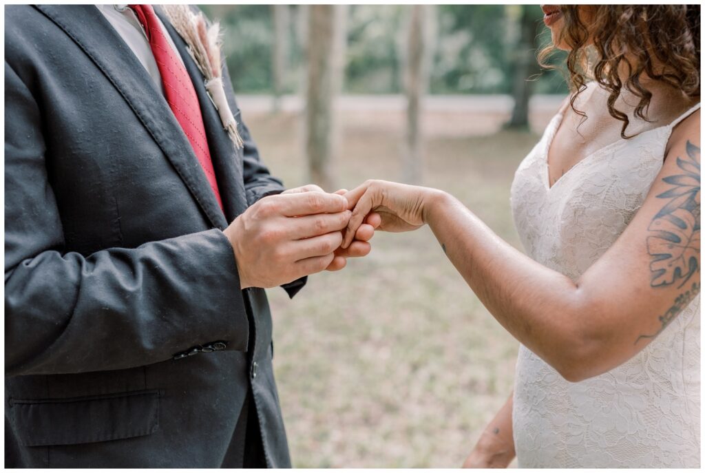 Close up image of Groom sliding wedding ring on Bride's finger.
