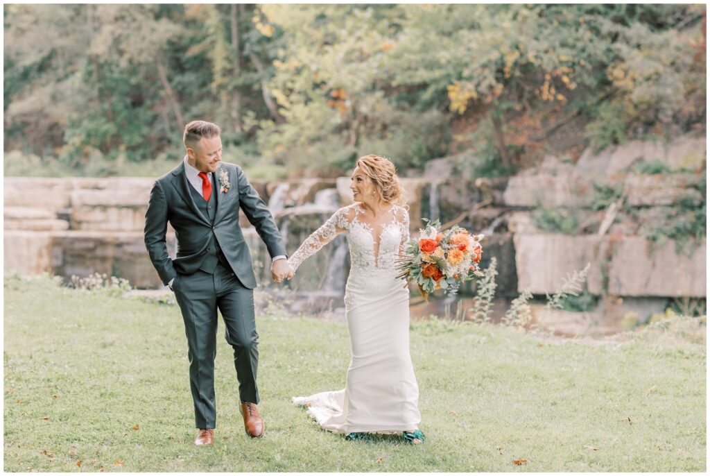 A couple walking hand in hand near a waterfall at Taughannock Falls State Park. This blog tells you everything you need to know on how to elope in Ithaca.
