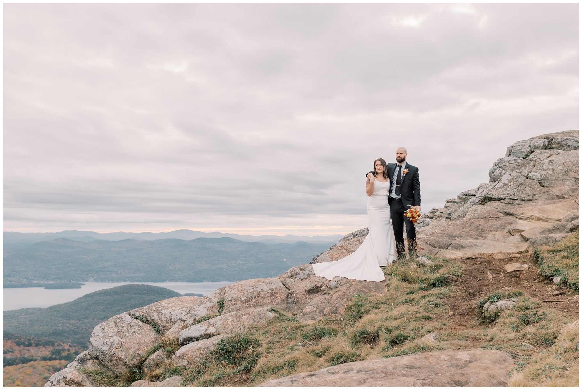 Bride and groom on top of a mountain looking out at the view of a mountain range.
