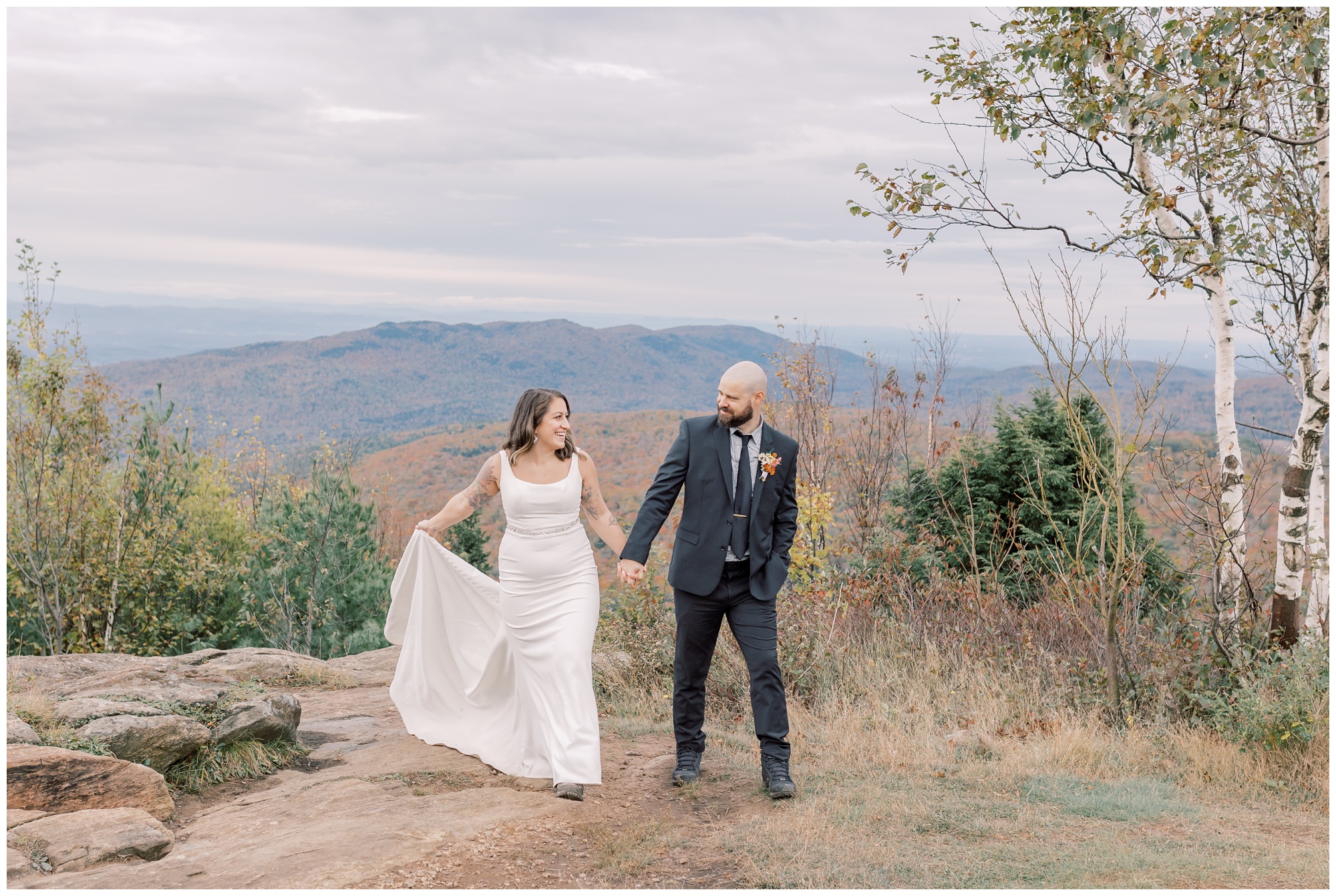 Portrait of a couple who was just married walking hand in hand on top of a mountain with a view covered with fall foliage in Lake George, NY.
