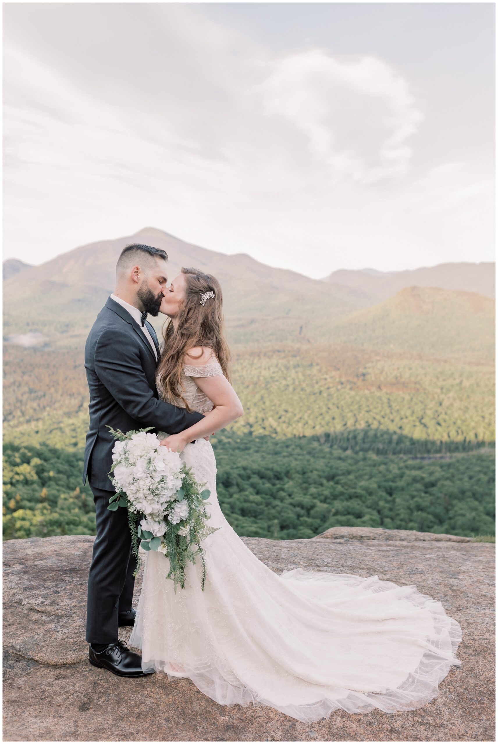 On a mountain top, a bride and groom kiss on their wedding day in Upstate New York during sunrise. 
