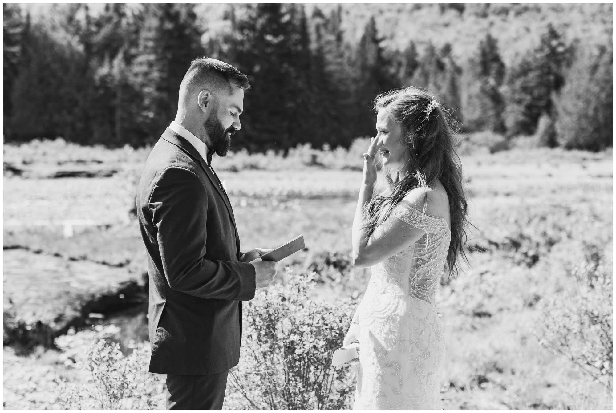 A bride wiping a tear while her groom says his vows. 
