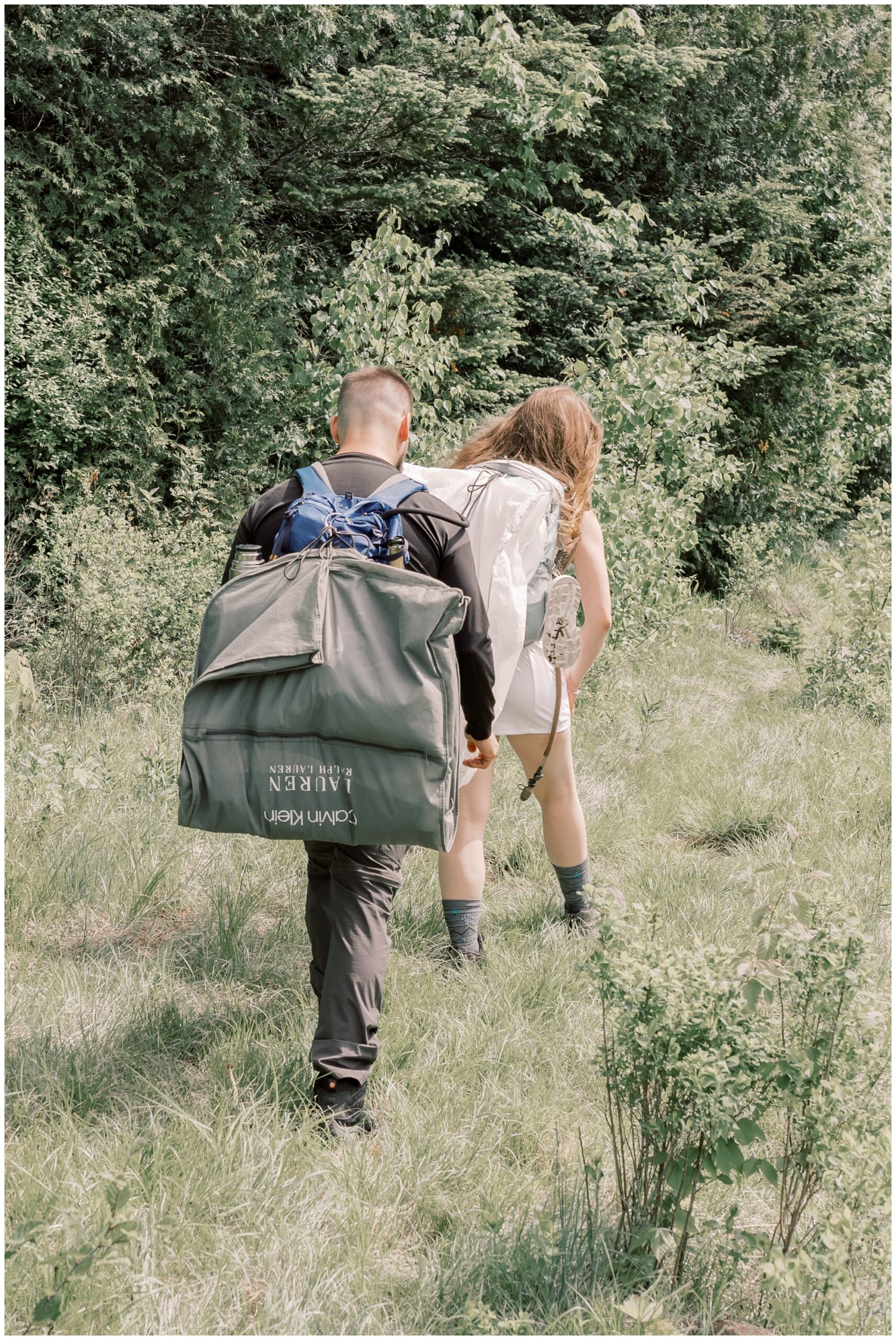 Man and Woman hiking while carrying their wedding attire. 
