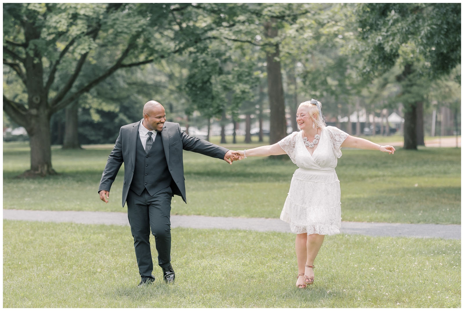 Mixed race couple walking through Saratoga Spa State Park on their wedding day. They are holding hands and smiling with Avenue of the Pine in the background.
