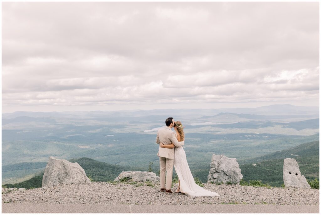 Bride and groom cuddled together looking at a view of Lake Placid on top of Whiteface mountain.