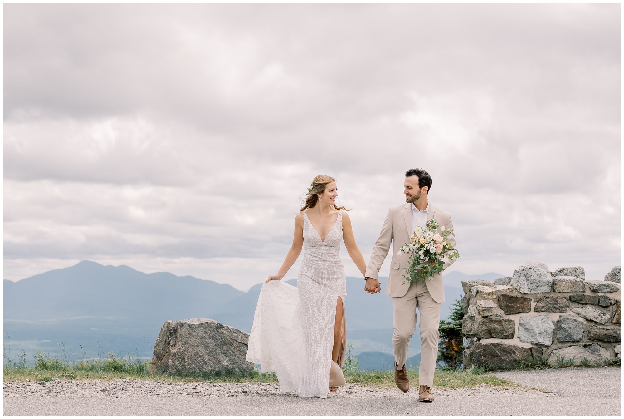 Bride and Groom holding hands and walking across the road at the top of Whiteface Mountain in the Adirondacks.