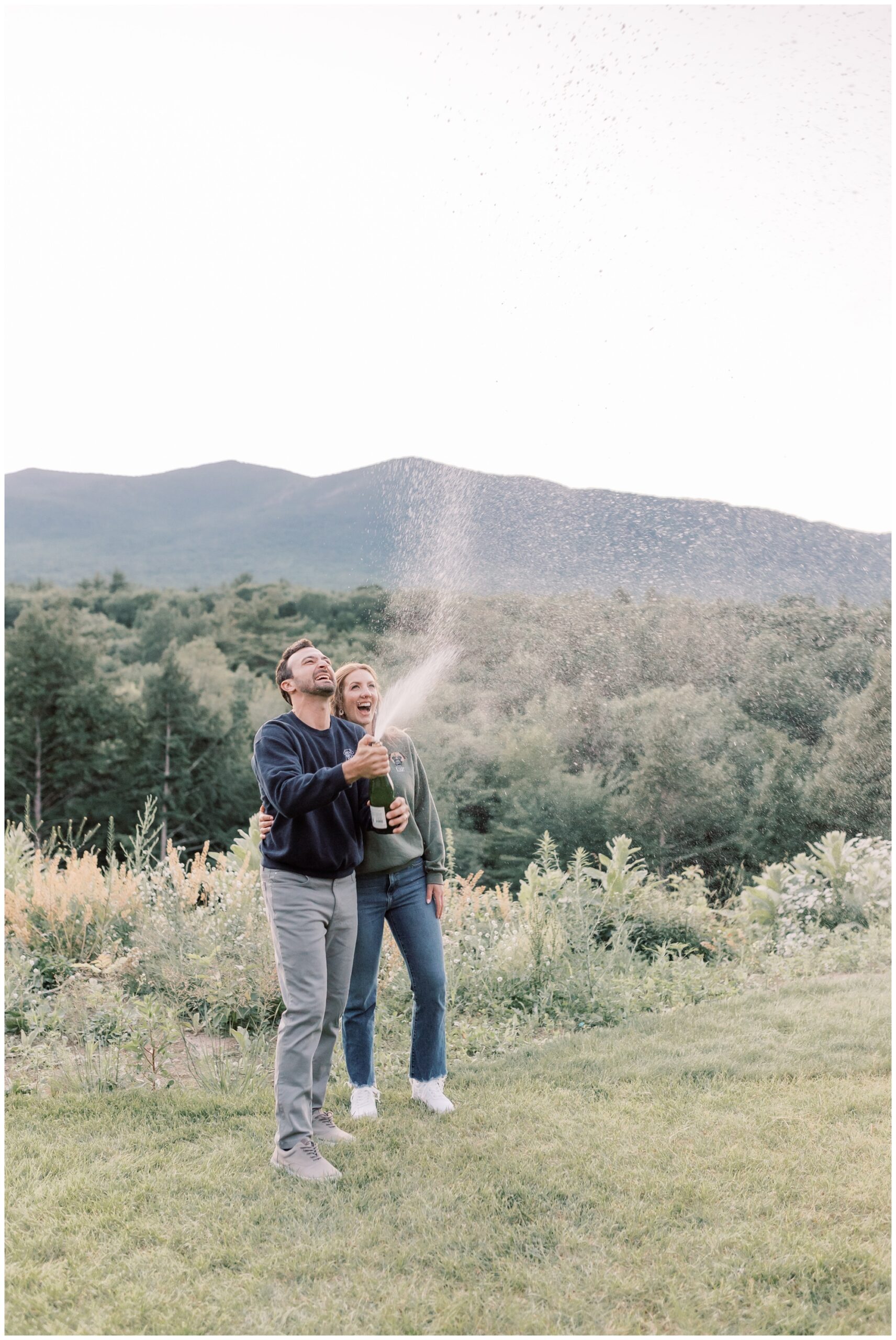 A couple spraying champagne during sunset with mountains in the background in celebration of their micro wedding in Lake Placid.
