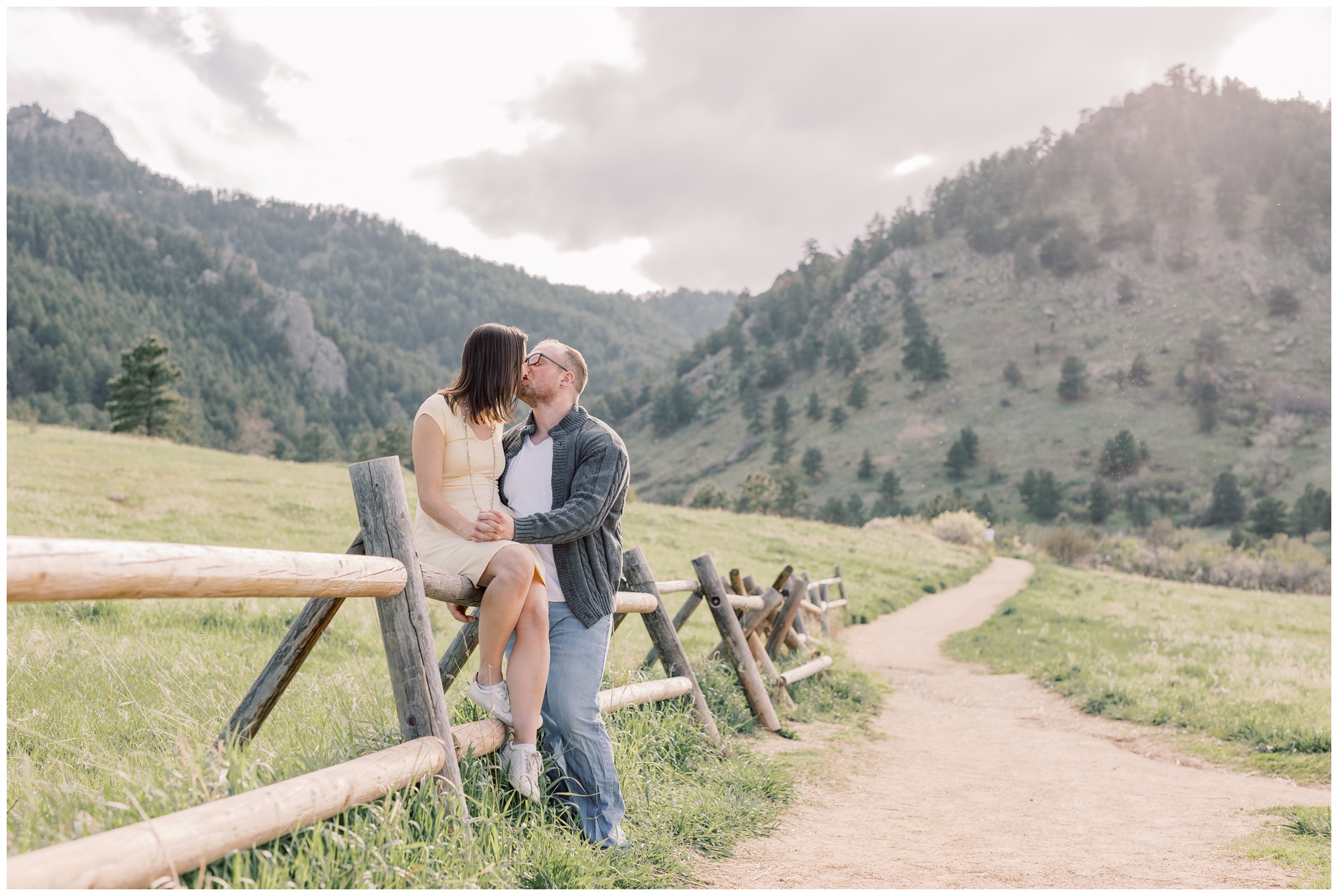 Woman kissing her husband while sitting on a wooden fence at the Flatirons in Colorado during their Boulder Anniversary Session.