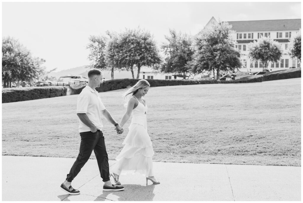 Black and white photo of an engaged couple walking hand and hand in front of The Sagamore hotel.