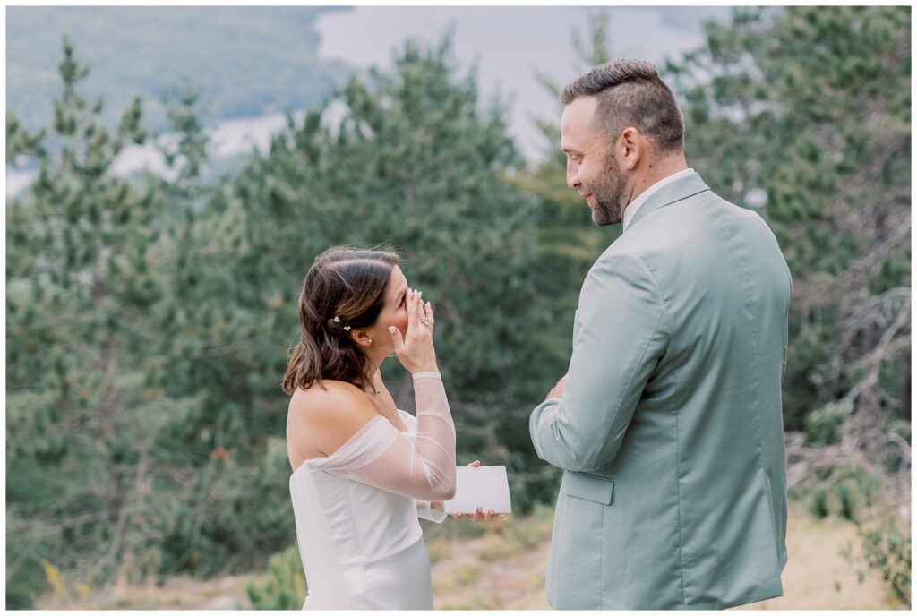 A bride and groom stand on a mountain as the bride wipes away tears during their ceremony. A secluded mountaintop ceremony is one way to make the most out of your elopement.