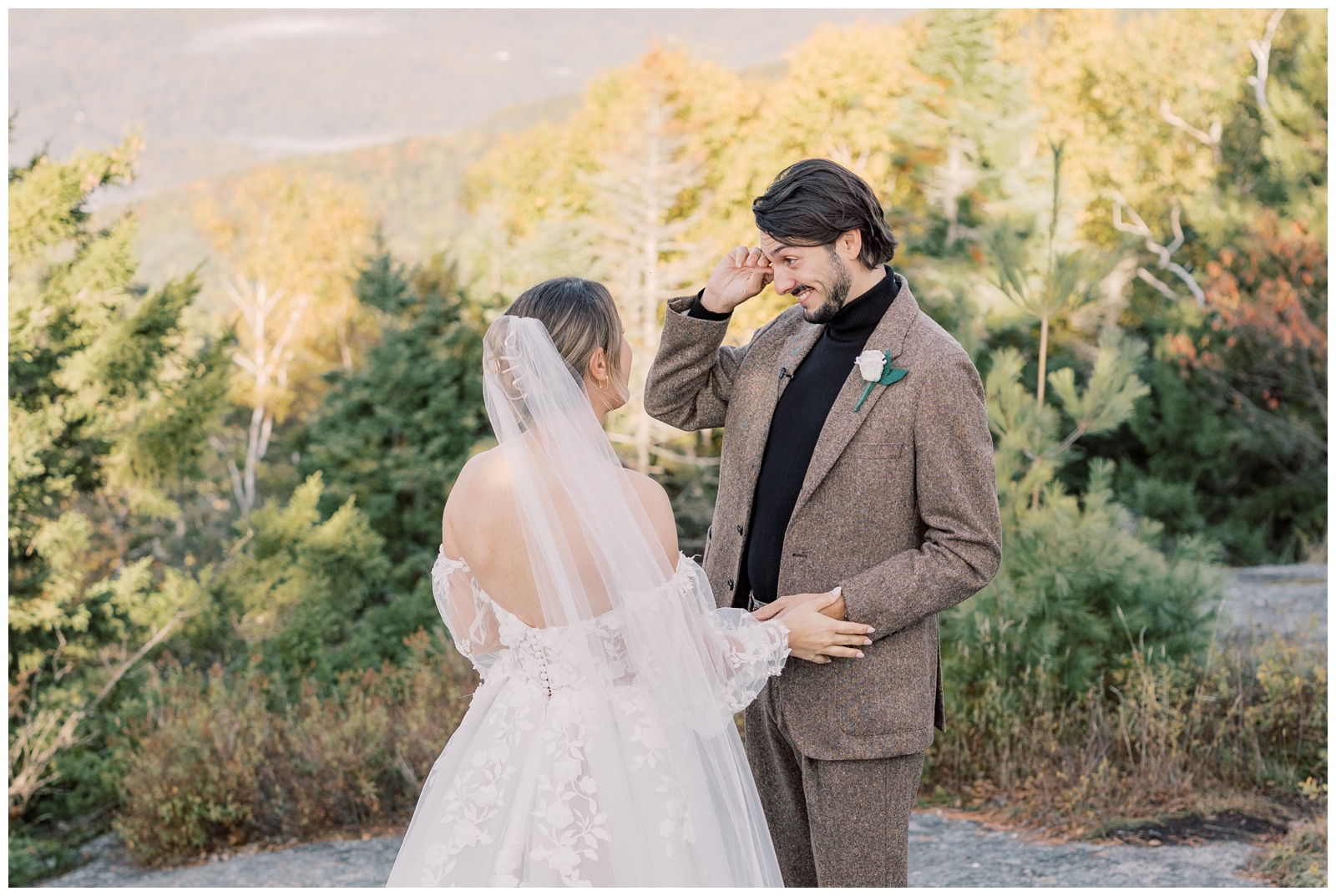 Groom in a brown suit wiping away tears while his bride embraces him.