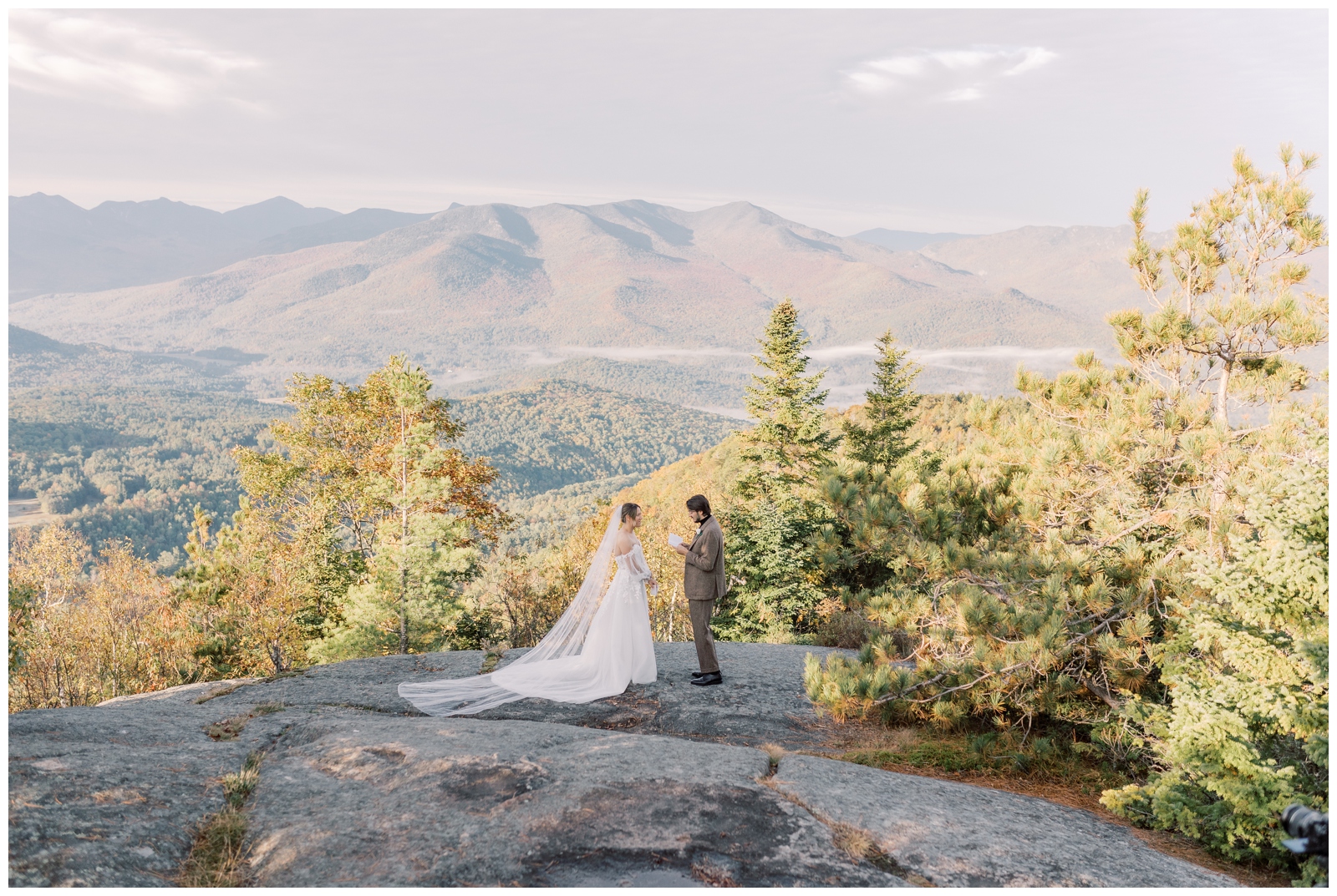 Couple standing on a mountain with a mountain range in the background reading their wedding vows to each other.
