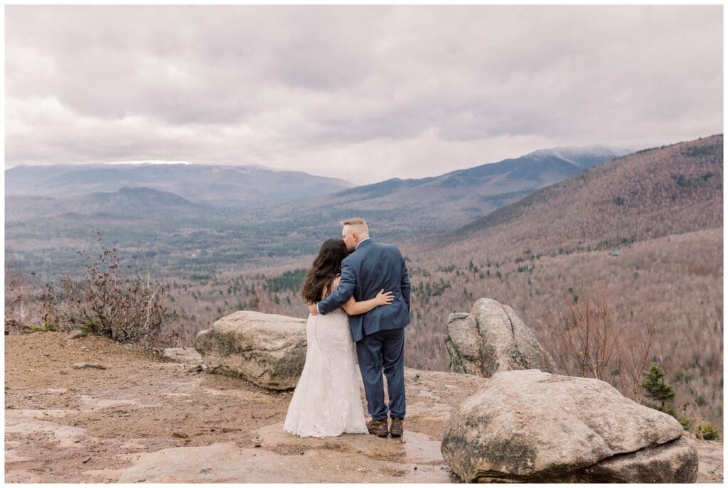 Couple standing at the peak of a mountain during their winter elopement in Lake Placid taking in the Adirondack snow covered view.