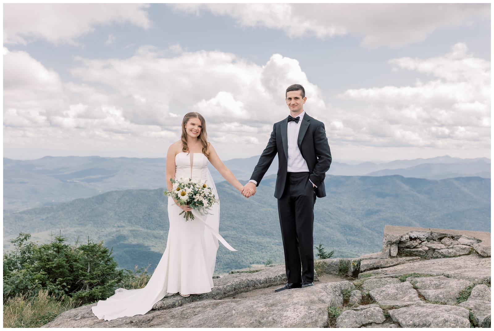 Bride and groom holding hands on Whiteface Mountain with sweeping Adirondack views.