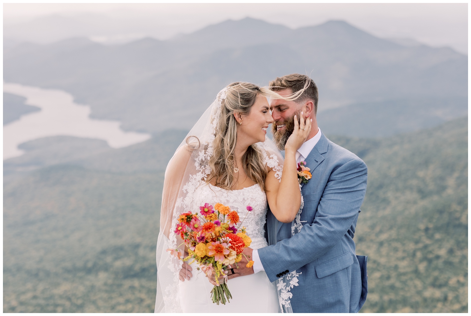 Bride and groom looking at each other on top of a mountain in the Adirondacks while her hair blows in the wind.