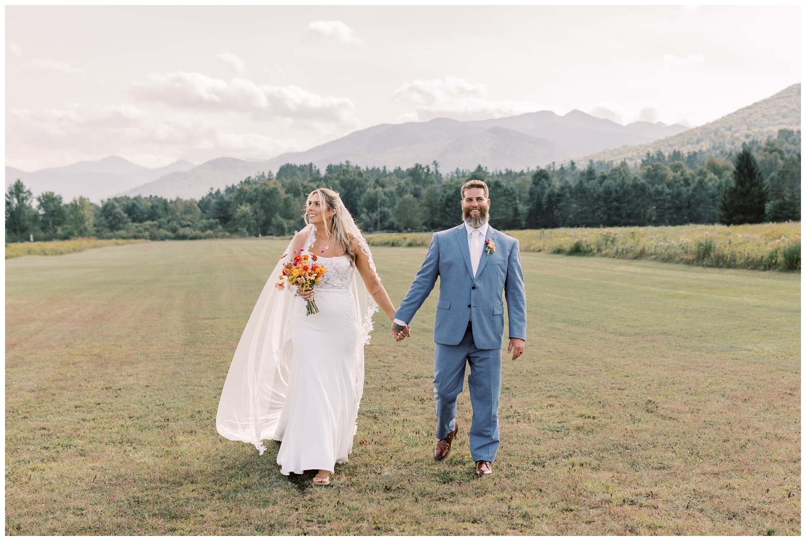 Bride and Groom holding hands while walking through Marcy Field with mountains in the background.