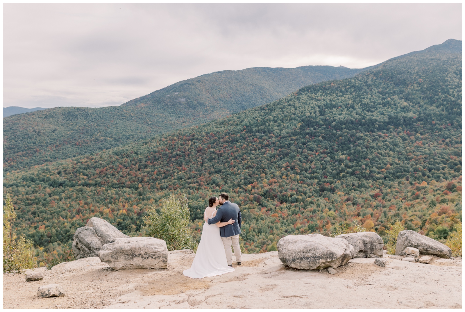Bride and groom kissing on the summit of a mountain overlooking whiteface in the Adirondacks in the Fall.